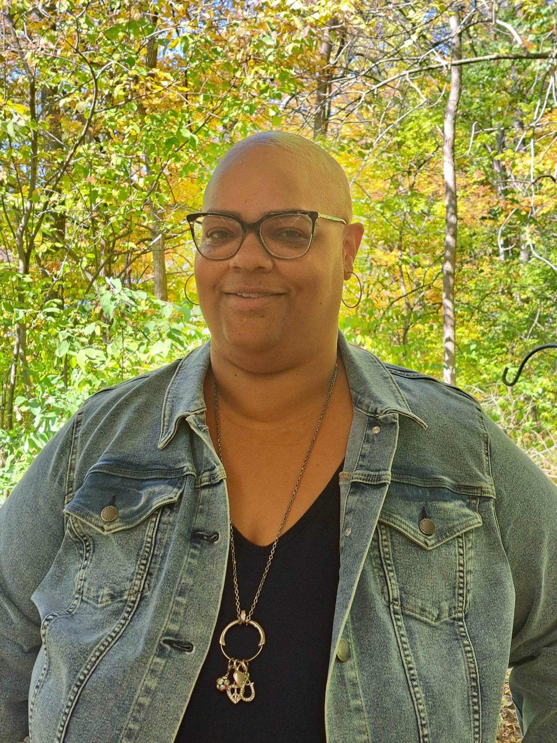 Anita Jackson smiling in a white shirt. Trees and shrubs behind her. 